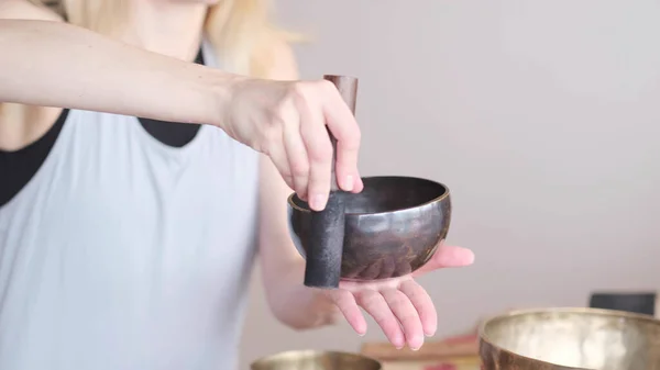 Woman playing on Tibetan singing bowl while sitting on yoga mat. Vintage tonned. — Stock Photo, Image