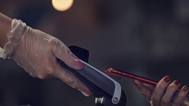 Ödeme terminali üzerinde akıllı telefonu tutan insan eli. Lastik eldivenli garson.