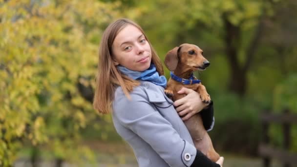 Lächelnde Dame, die sich Zeit mit ihrem Hund nimmt. Frau entspannt sich in der Natur mit ihrem kleinen Hund. Sie kratzt sich am Rücken. Hund leckt seiner Besitzerin Nase. Zeitlupe in Großaufnahme — Stockvideo