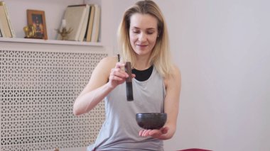 Kadın yoga minderinde otururken Tibet şarkı kasesinde oynuyor. Klasik tonlama.