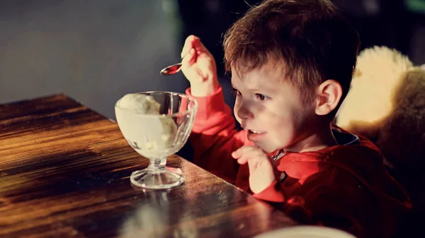 Um rapazinho a comer gelado no café. Criança bonita, desfrutando de iogurte de baunilha em um restaurante — Fotografia de Stock