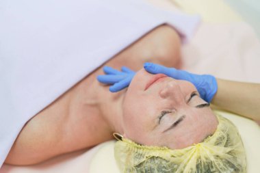 Cilt bakımından hoşlanan, gözleri kapalı, çekici bir kadının portresi. Masöz kolları müşterinin çenesine ve burnuna dokunuyor. Yaşlanma karşıtı etki