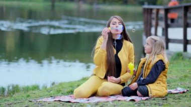 Park 'taki mutlu aile. Tatlı dişi çocuk çorba köpüğü üflüyor ve annesiyle birlikte doğada köpük yapıyor. Sonbahar parkı, birlikte zaman geçirmek. Aile zamanı. Yakın çekim videosu. Yavaş çekim görüntüleri