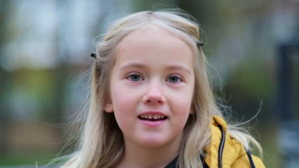 Ritratto di una bella bambina che tiene in mano un fiore di trifoglio. ragazza carina 5 anni occhi astuti guardando altrove con un sorriso guardare la fotocamera. chiudi Video girato. Video al rallentatore — Video Stock