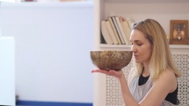 Kadın yoga minderinde otururken Tibet şarkı kasesinde oynuyor. Antika tonlu. Stok görüntüleri. Slow Motion videosu. Kapat.