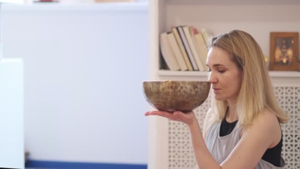 Žena hraje na tibetské pěvecké míse, zatímco sedí na podložce na jógu. Ročník tonizován. Záběry ze skladu. Zpomalené video. Zavřít — Stock video