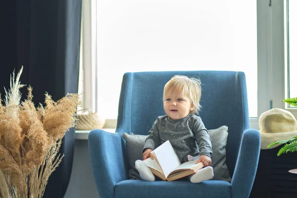 Infant child baby girl toddler sitting and reading book on the sofa in the living room. portrait — Stock Photo, Image