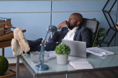 Rahatlamış işçiler işlerini bitirdikten sonra sıkı çalışma günlerinden sonra işi bırakırlar. Düşünceli Afro-Amerikan işadamı pencereden dışarı bakıyor ve ofis masasında oturuyor..