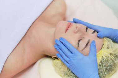 Cilt bakımından hoşlanan, gözleri kapalı, çekici bir kadının portresi. Masöz kolları müşterinin çenesine ve burnuna dokunuyor. Yaşlanma karşıtı etki