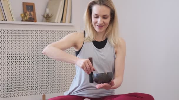 Vrouw die op een Tibetaanse zangkom speelt terwijl ze op een yogamat zit. Vintage tonned. Beelden. Slow Motion video. Sluiten. — Stockvideo