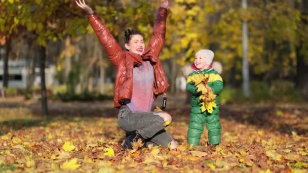 Filmagem 4k de menino com a mãe coletando e colhendo folhas de outono douradas no parque tiro em câmera lenta. — Vídeo de Stock