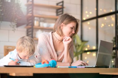 Anne, küçük oğluna dizüstü bilgisayarda yardım ediyor. Küçük çocuğa bilgisayar kullanmayı öğreten genç bir kadın. Bebek bakıcısı küçük kıza laptop uygulaması kullanmayı öğretiyor.