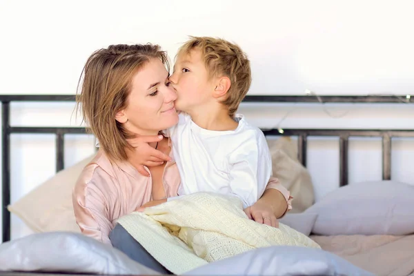 Krásná žena a její roztomilý malý syn se objímají a usmívají. Chlapec líbá svou mámu na tvář — Stock fotografie