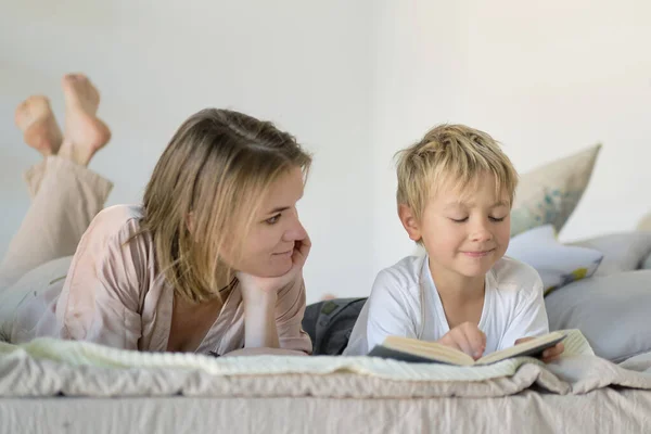 Máma učí syna číst knihu, je doma na posteli. Vzdělávací koncepty. Pastelové barvy, selektivní zaměření. — Stock fotografie