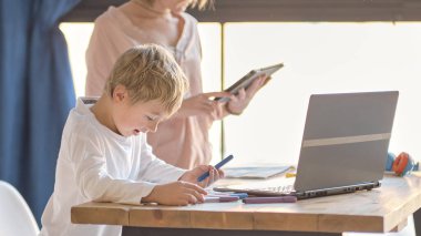 Anne, küçük oğluna dizüstü bilgisayarda yardım ediyor. Küçük çocuğa bilgisayar kullanmayı öğreten genç bir kadın. Bebek bakıcısı küçük kıza laptop uygulaması kullanmayı öğretiyor.