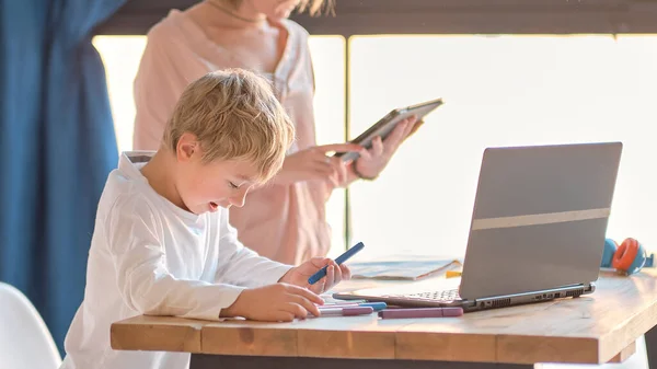 Mama pomaga młodemu synowi z laptopem odrabiać lekcje. Młoda kobieta uczy małego chłopca korzystać z komputera. opiekunka do dziecka uczy małe dziecko dziewczynka używać laptopa aplikacji. — Zdjęcie stockowe