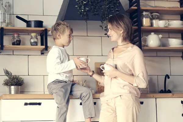 young mom and son look at each other. Happy family in the morning. Beautiful woman with her son having breakfast in kitchen together, son looking at mother and smiling
