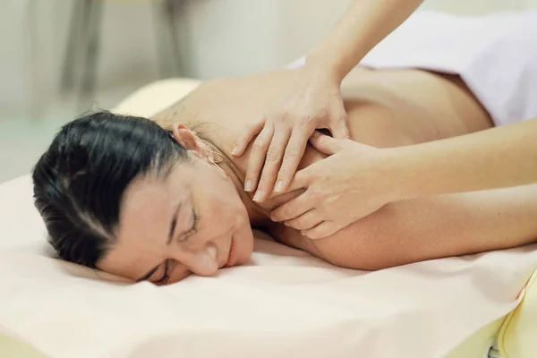 Fisioterapista che massaggia la schiena e la spalla di una paziente. Vista sulla spalla del massaggiatore che esegue un massaggio profondo dei tessuti della schiena delle donne per liberare il dolore — Foto Stock