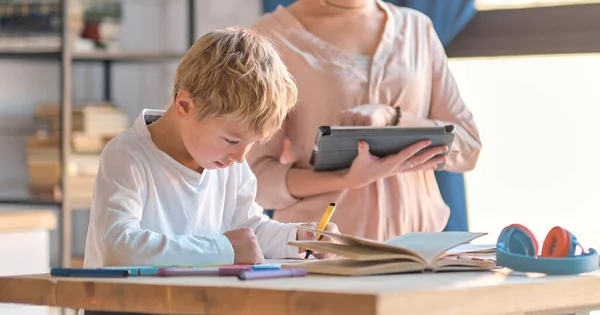 Mamá ayudando a su hijo pequeño con el ordenador portátil para hacer la tarea. Mujer joven enseñando a un niño a usar la computadora. niñera enseñando niña pequeña uso de la aplicación portátil. —  Fotos de Stock