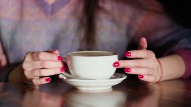Ahşap masada latte taşıyan kadın elleri. Kırmızı tırnaklı kadın elinde kahve tutuyor..