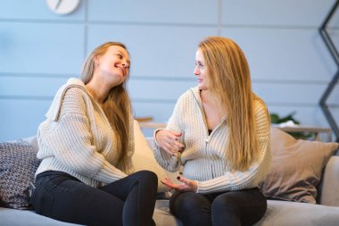 Anne ve yetişkin kız oturma odasında kanepede oturup eğleniyorlar. Mutlu, olgun bir anne ve milenyum kızı. Evdeki kanepede oturup sohbet ediyorlar ve gülüyorlar.