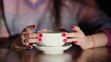Ahşap masada latte taşıyan kadın elleri. Kırmızı tırnaklı kadın elinde kahve tutuyor..