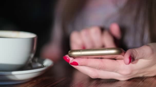 Hand einer Frau, die nach einer Kaffeetasse greift, während sie SMS in ihr Smartphone schreibt. Frau sitzt im Café, trinkt Kaffee und telefoniert — Stockvideo