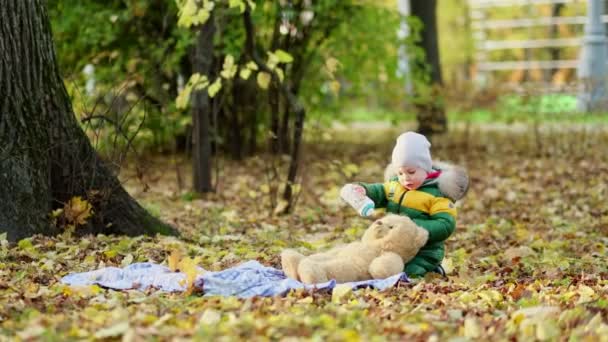 Un ragazzino che gioca con un peluche nel parco. divertente bambino otty in un caldo piumino e il suo orsacchiotto. vista da vicino. Video al rallentatore. stock di filmati — Video Stock