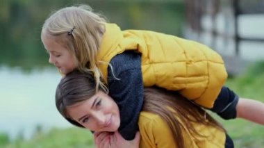 Güzel ve mutlu genç anne, gülen kızını sırtında taşıyor. Yavaş çekim videosu. depolama görüntüleri