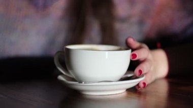 Ahşap masada latte taşıyan kadın elleri. Kırmızı tırnaklı kadın elinde kahve tutuyor..