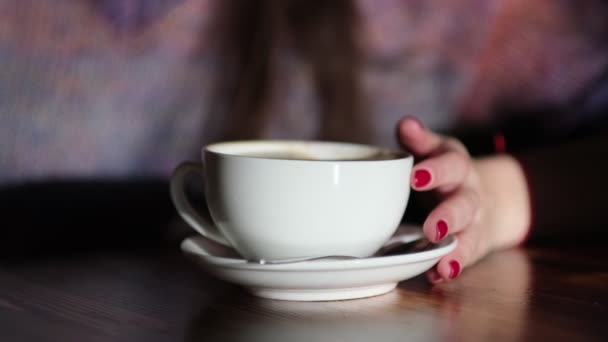 Γυναίκα χέρια με latte σε ένα ξύλινο τραπέζι. γυναίκα με κόκκινα νύχια κρατά τον καφέ στα χέρια της. — Αρχείο Βίντεο