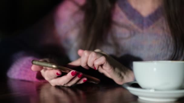 Hand einer Frau, die nach einer Kaffeetasse greift, während sie SMS in ihr Smartphone schreibt. Frau sitzt im Café, trinkt Kaffee und telefoniert — Stockvideo