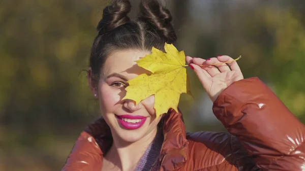 Szczęśliwy uśmiechnięta kobieta trzyma w dłoniach żółty klon liście przykrywające jej oko na jesień natura tło — Zdjęcie stockowe
