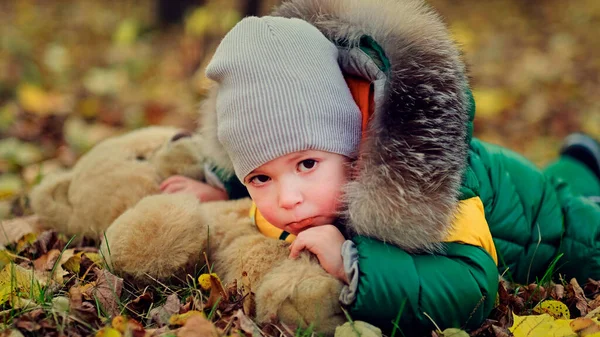 Menino brincando com um brinquedo de pelúcia no parque. engraçado bebê otty em um casaco quente e seu ursinho de pelúcia. vista de perto — Fotografia de Stock