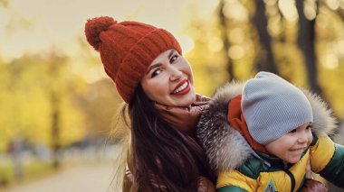 Güzel genç anne ve küçük oğlu parkta eğleniyor. Aile doğa yürüyüşünün tadını çıkarıyor. Mutlu annelik kavramı.