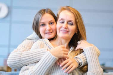 Anne ve kızının güzel bir ailesi var, evde sarılıp öpüşüyorlar. Büyük anne ve yetişkin kızı sarılıyor, kameraya bakıyor ve gülümsüyor.