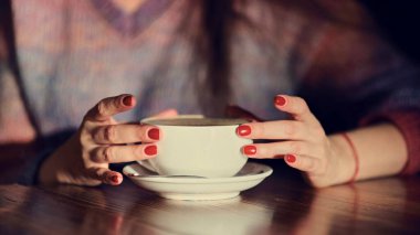 Ahşap masada latte taşıyan kadın elleri. Kırmızı tırnaklı kadın elinde kahve tutuyor..