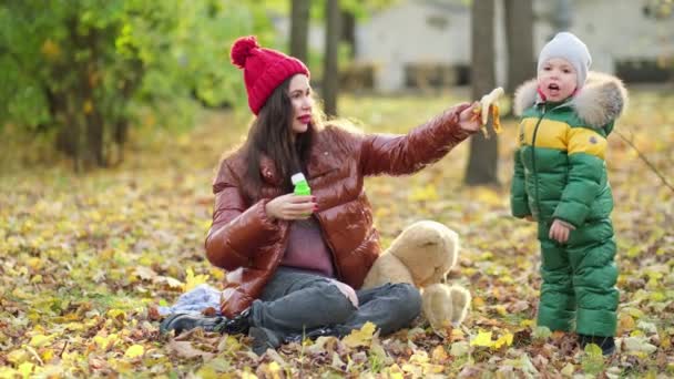 Giovane mamma o tata stanno giocando nel parco. Mamma soffia bolle di sapone. passeggiata in autunno sulla natura. famiglia felice. vista da vicino. Video al rallentatore. stock di filmati — Video Stock