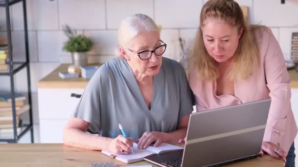 Žena, která učí starší matku používat internet doma. Starší žena se svou dcerou se dívají na moderní gadget uvnitř. pohled zblízka. Zpomalit na video. stock záběry — Stock video