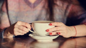 ženské ruce s latté na dřevěném stole. žena s červenými nehty drží kávu v rukou.