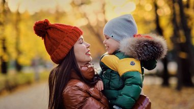 Güzel genç anne ve küçük oğlu parkta eğleniyor. Aile doğa yürüyüşünün tadını çıkarıyor. Mutlu annelik kavramı. yumuşak odak