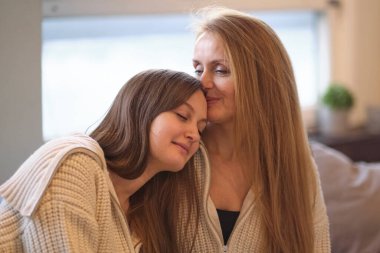 Anne ve yetişkin kız oturma odasında kanepede oturup eğleniyorlar. Mutlu, olgun bir anne ve milenyum kızı. Evdeki kanepede oturup sohbet ediyorlar ve gülüyorlar.