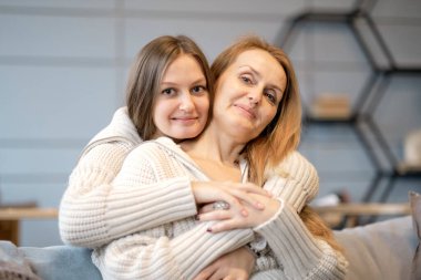 Anne ve kızının güzel bir ailesi var, evde sarılıp öpüşüyorlar. Büyük anne ve yetişkin kızı sarılıyor, kameraya bakıyor ve gülümsüyor.