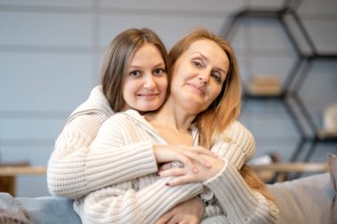 Beautiful family of mother and daughter together, hugging and kissing at home. senior mom and her adult daughter are hugging, looking at camera and smiling clipart