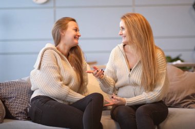 Neşeli genç bir kadın, yaşlı bir anneye sarılıyor. Oturma odasında dinlenirken koltukta oturuyor. Mutlu anne ve arkadaş canlısı kız el ele tutuşup birbirlerine bakıyorlar..