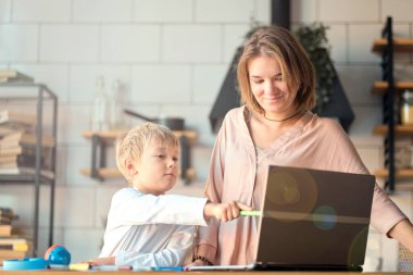 Anne, küçük oğluna dizüstü bilgisayarda yardım ediyor. Küçük çocuğa bilgisayar kullanmayı öğreten genç bir kadın. Bebek bakıcısı küçük kıza laptop uygulaması kullanmayı öğretiyor.