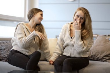 Mutlu anne ve arkadaş canlısı kız el ele tutuşup birbirlerine bakıyorlar. Anne yetişkin kız kanepede oturmuş gülümsüyor. Sarılmak mutlu hissettiriyor. Birlikte vakit geçirmek. Sevgi kavramı.