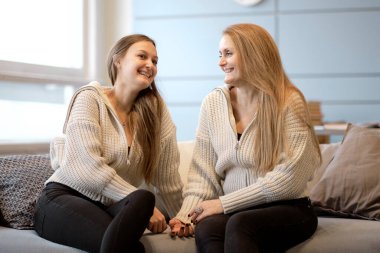 Anne ve yetişkin kız oturma odasında kanepede oturup eğleniyorlar. Mutlu, olgun bir anne ve milenyum kızı. Evdeki kanepede oturup sohbet ediyorlar ve gülüyorlar.