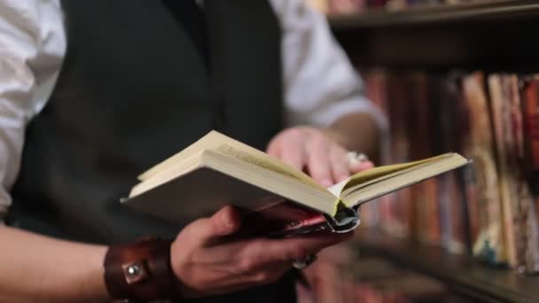 Tyylikkäästi pukeutunut mies selailee vintage-kirjoja vanhassa pimeässä kirjastossa. lähikuva. — kuvapankkivideo