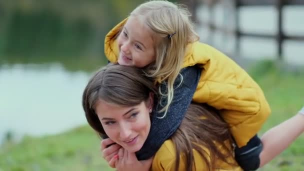 Bela e feliz jovem mãe dando passeio de piggyback para sua filha rindo. Vídeo em câmara lenta. imagens de stock — Vídeo de Stock